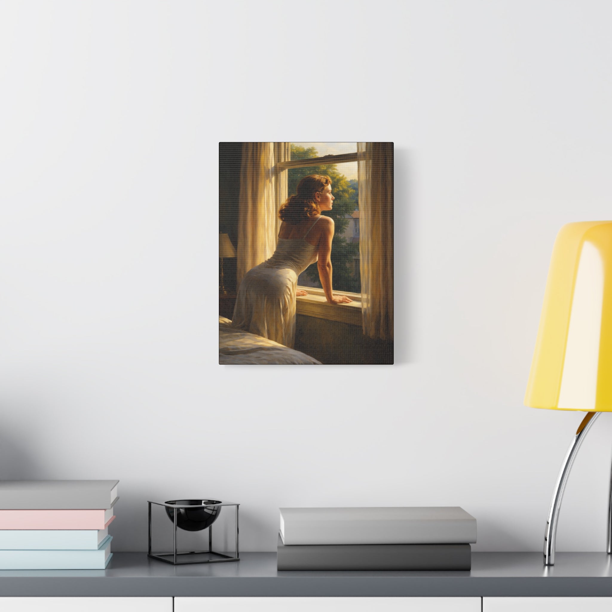 Canvas print of a woman by a window on a wall above a desk with books and a lamp.